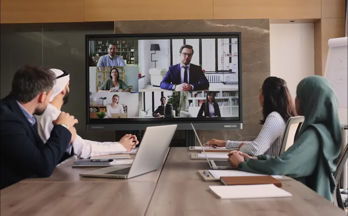 Diverse technology team collaborating in a bright modern meeting room with laptops and a large video screen